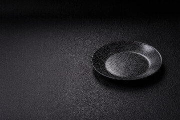 Empty round black plate for food, kitchen utensils on dining table. Empty plate
