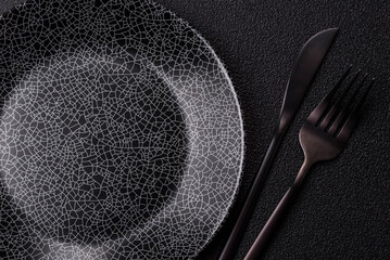 Empty round black plate for food, kitchen utensils on dining table. Empty plate