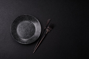 Empty round black plate for food, kitchen utensils on dining table. Empty plate