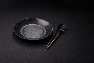 Empty round black plate for food, kitchen utensils on dining table. Empty plate
