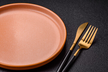 Empty round black plate for food, kitchen utensils on dining table. Empty plate