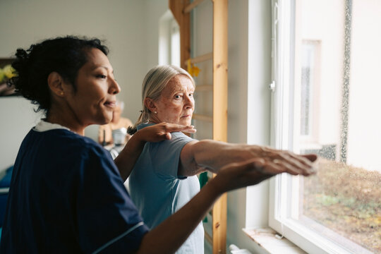 Female therapist helping senior woman with stretching exercise at rehabilitation center