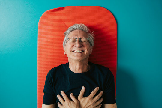 Directly above shot of happy man with hands on chest lying on exercise mat