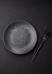 Empty round black plate for food, kitchen utensils on dining table. Empty plate