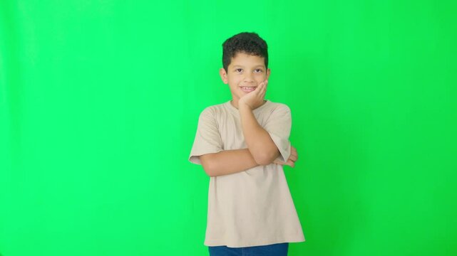 A young boy is standing in front of a green wall, looking down
