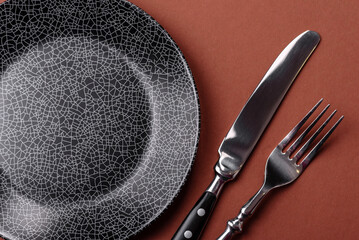 Empty round black plate for food, kitchen utensils on dining table. Empty plate