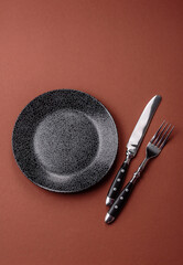 Empty round black plate for food, kitchen utensils on dining table. Empty plate