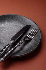Empty round black plate for food, kitchen utensils on dining table. Empty plate