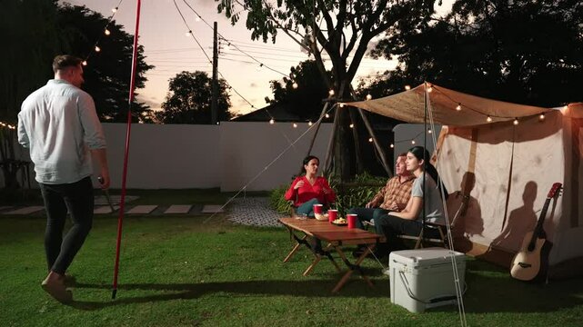 Family all together camp in garden, Father serve grilled food for family member. Outdoor camping activity to relax with nature and spend time with young generation cross generation gap. Divergence.