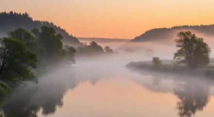 Fototapeta premium Foggy morning river valley surrounded by green hills, evoking calm and tranquility.