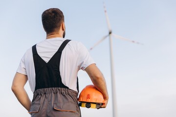 Engineer looking at a wind turbine holding an orange helmet