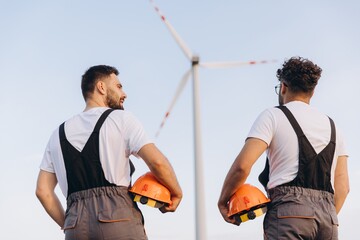 Engineers holding helmets looking at wind turbine in the desert