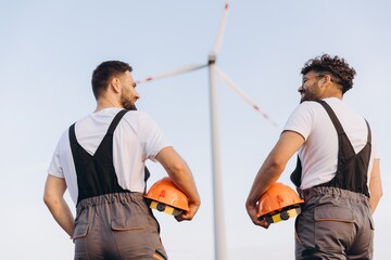 Engineers holding helmets and admiring a wind turbine