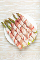 Delicious asparagus wrapped in bacon strips, seasoned with colorful peppercorns, presented on a white plate, ready to be cooked