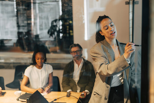 Businesswoman explaining strategies to team over television screen in meeting