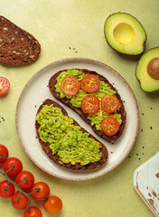 Slices of whole grain rye bread with mashed avocado, green peas and cherry tomatoes seasoned with...