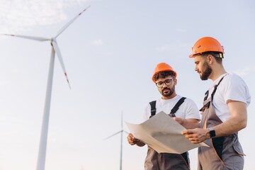 Engineers examining blueprints at wind turbine farm for sustainable energy