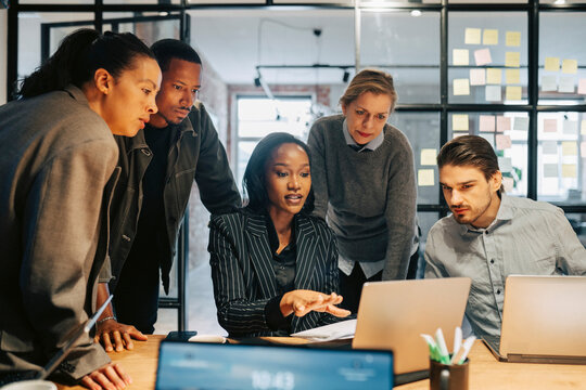 Businesswoman explaining strategies to team over laptop in office meeting room
