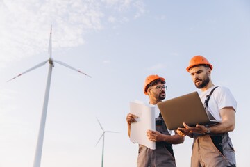 Engineers working on a wind turbine project using a laptop and blueprints