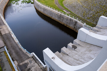 Top view of a curved concrete dam structure and canal with still water. Symmetrical modern...