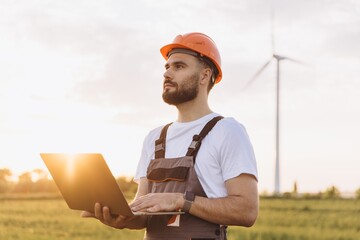 Engineer working with laptop in a wind turbine power plant at sunset