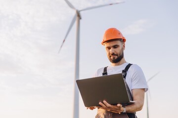Engineer working with laptop in wind turbine farm for sustainable energy