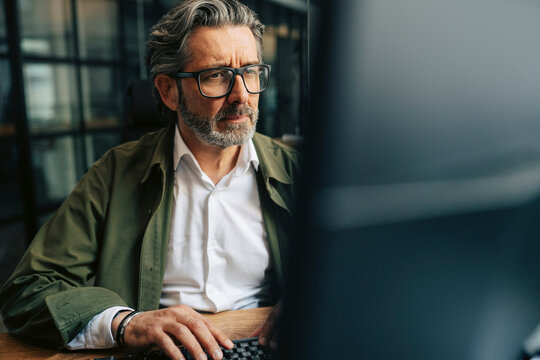 Pensive senior businessman working on computer at office