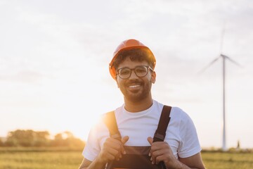 Arab engineer smiling in front of wind turbine at sunset