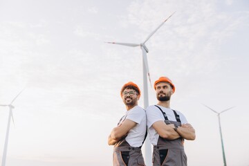 Arab engineers standing back to back with arms crossed in a wind turbine power plant