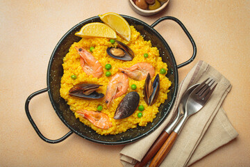 Seafood paella with rice, shrimp, mussels, peas, and lemon wedges served in a black traditional pan...