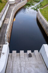 Hydropower canal with calm water viewed from above. Concrete steps of a dam or floodgate visible in...
