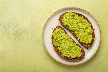 Mashed avocado seasoned with sesame seeds is spread on two slices of toasted rye bread, served on a...