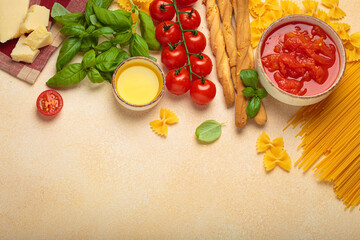Ingredients for cooking Italian dish. Tomato sauce, grissini, farfalle pasta, spaghetti, fresh tomatoes, basil, parmesan cheese, and olive oil on light beige background, copy space