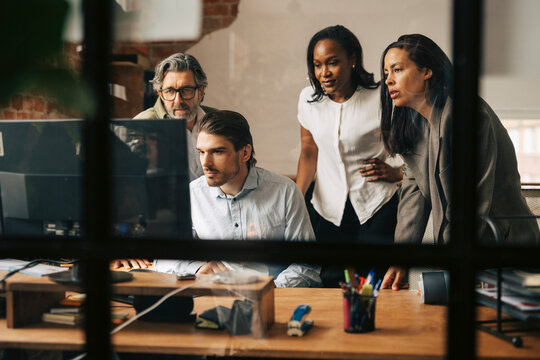 Team of focused entrepreneurs working on computer seen through glass