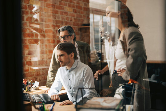 Group of corporate professionals working together at office seen through glass