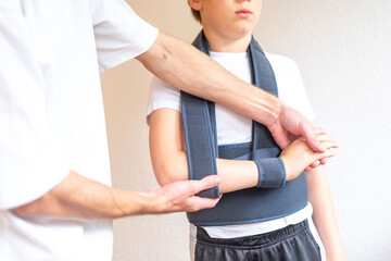 Teen boy in an orthopedic sling, Medical professional fitting therapeutic support belt on patient...
