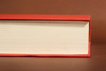 Detail of a Book with Red Cover and Cream Pages on Brown Background
