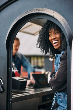 Happy mature female owner with curly hair standing near door of food truck