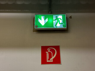 Emergency exit sign with illuminated green arrow and running figure, positioned above fire...