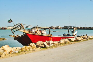 A red boat is sitting on the shore of a body of water