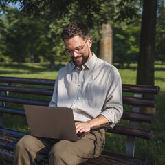 Adult businessman sit on bench in a public park and use laptop