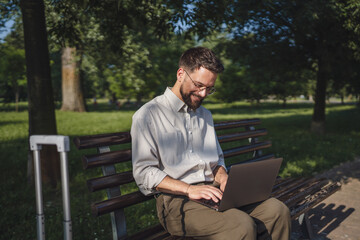 Adult businessman sit on bench in a public park and use laptop
