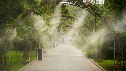 Outdoor air cooling system (fogging) in extreme heat. Spraying moisture over the road with pedestrians in the distance.