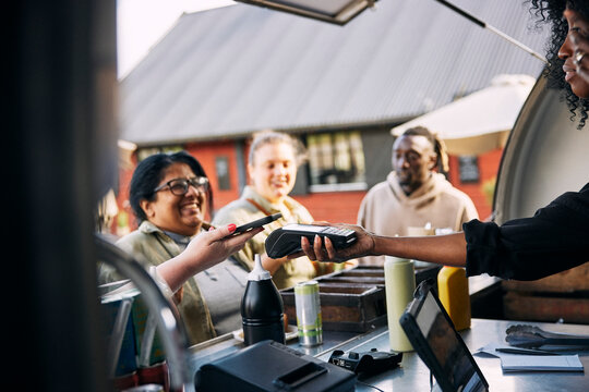 Customer using smart phone for making payment through tap to pay method on credit card reader at food truck