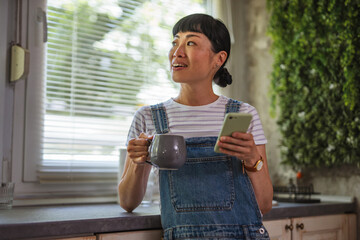 Japanese woman drink coffee and use mobile phone in a kitchen