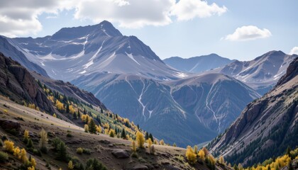 the image is a landscape view of several mountains under a partly cloudy sky. the foreground features a slope covered in short grass, boulders, and a scattering of trees