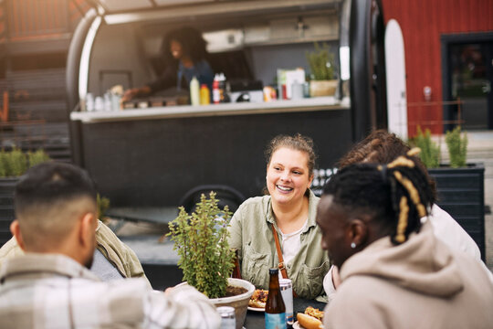 Smiling young woman spending leisure time with friends having hot dog at street near food truck