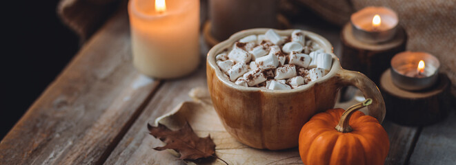 Spicy sweet fall hot drink: delicious pumpkin latte with cinnamon, marshmallow with salted caramel. Served in handmade artisan mug in shape of pumpkins, cozy home decor with candles, dry autumn leaves