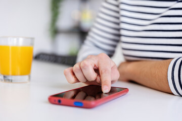 Unrecognizable young woman browsing on her smart phone at home while drinking a glass of orange...