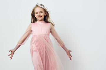 Cheerful young girl in a pink dress smiling joyfully, with flowing hair, against a soft pastel...